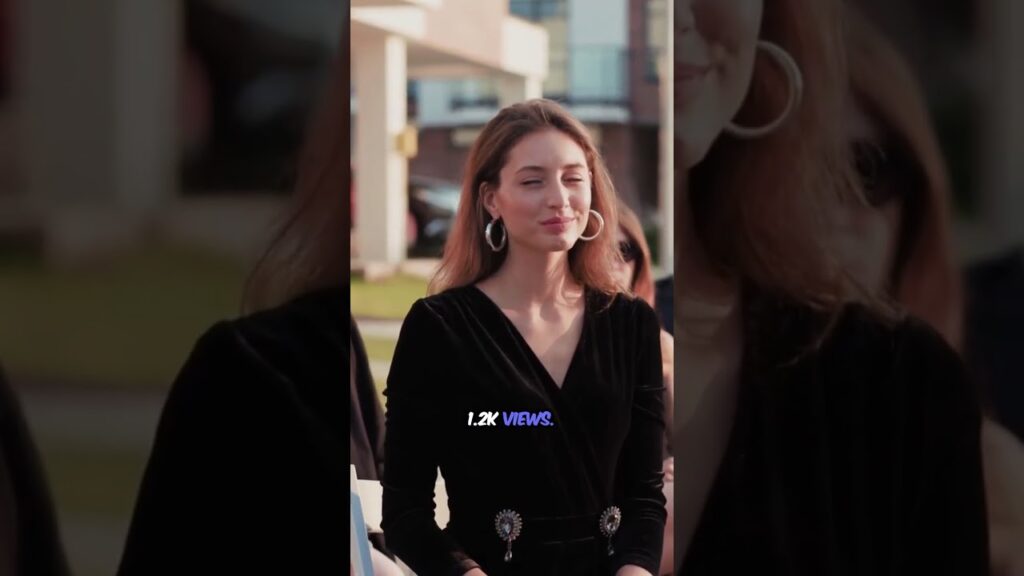 Woman wearing a black dress with large earrings, smiling outdoors in a casual setting.